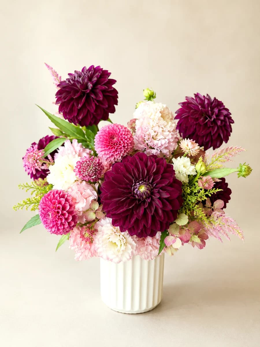 The Delphine - lush arrangement of plum and pink dahlias, pompons, and antique hydrangea in a white ribbed vase