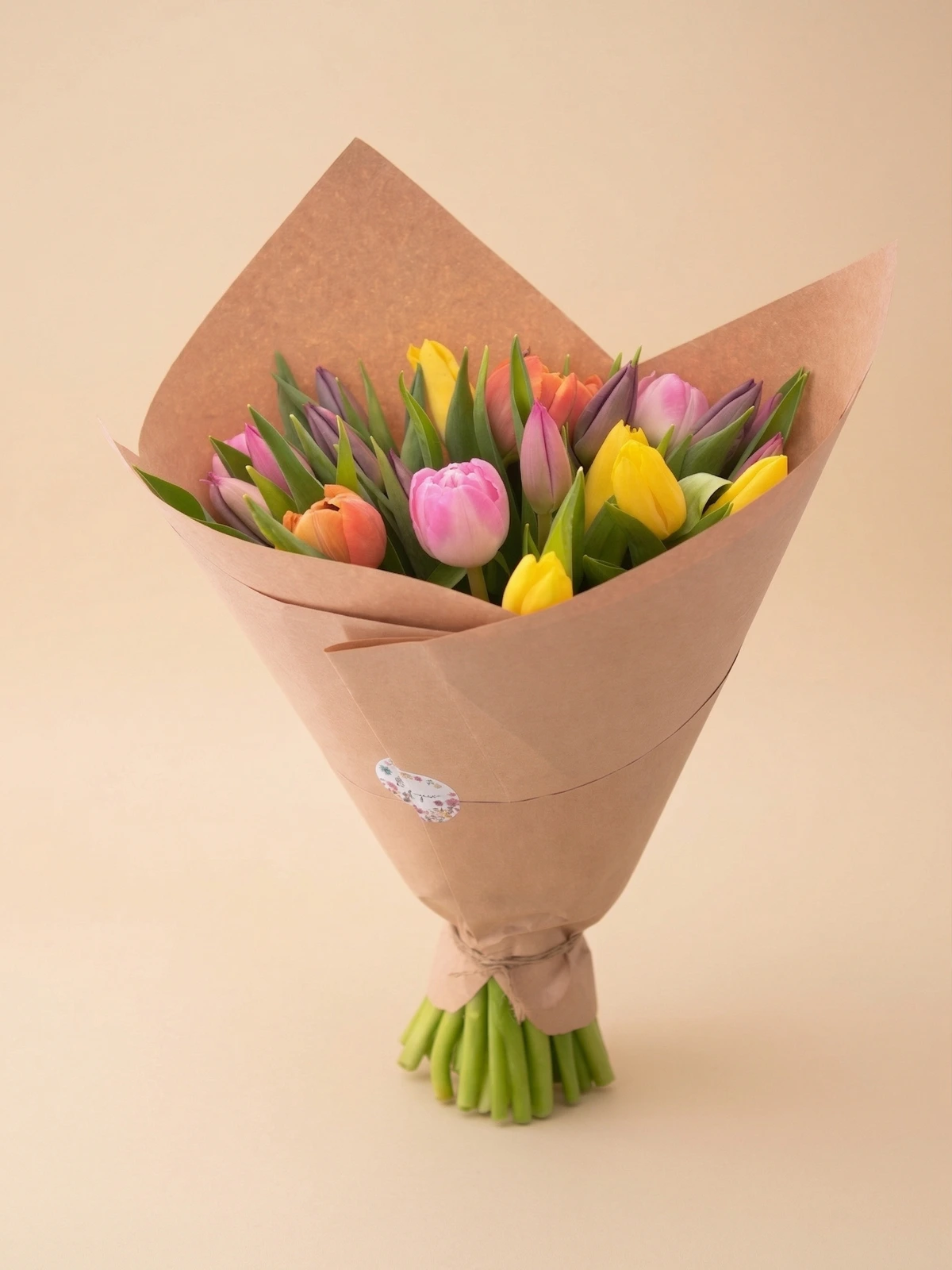 The Colette - hand-tied spring tulip bouquet in natural kraft paper with pink, yellow, coral, and purple tulips
